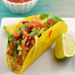 healthy fish taco on a white plate with a wedge of lemon