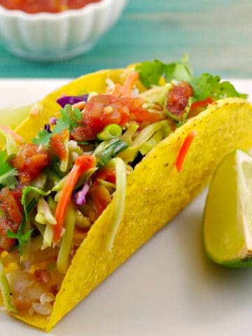 healthy fish taco on a white plate with a wedge of lemon