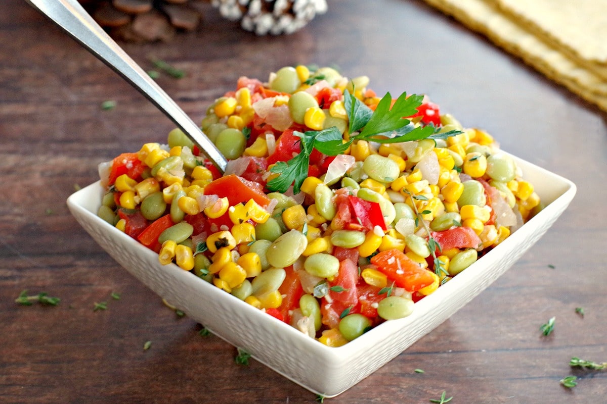 corn succotash in a white bowl with pine cones in the background