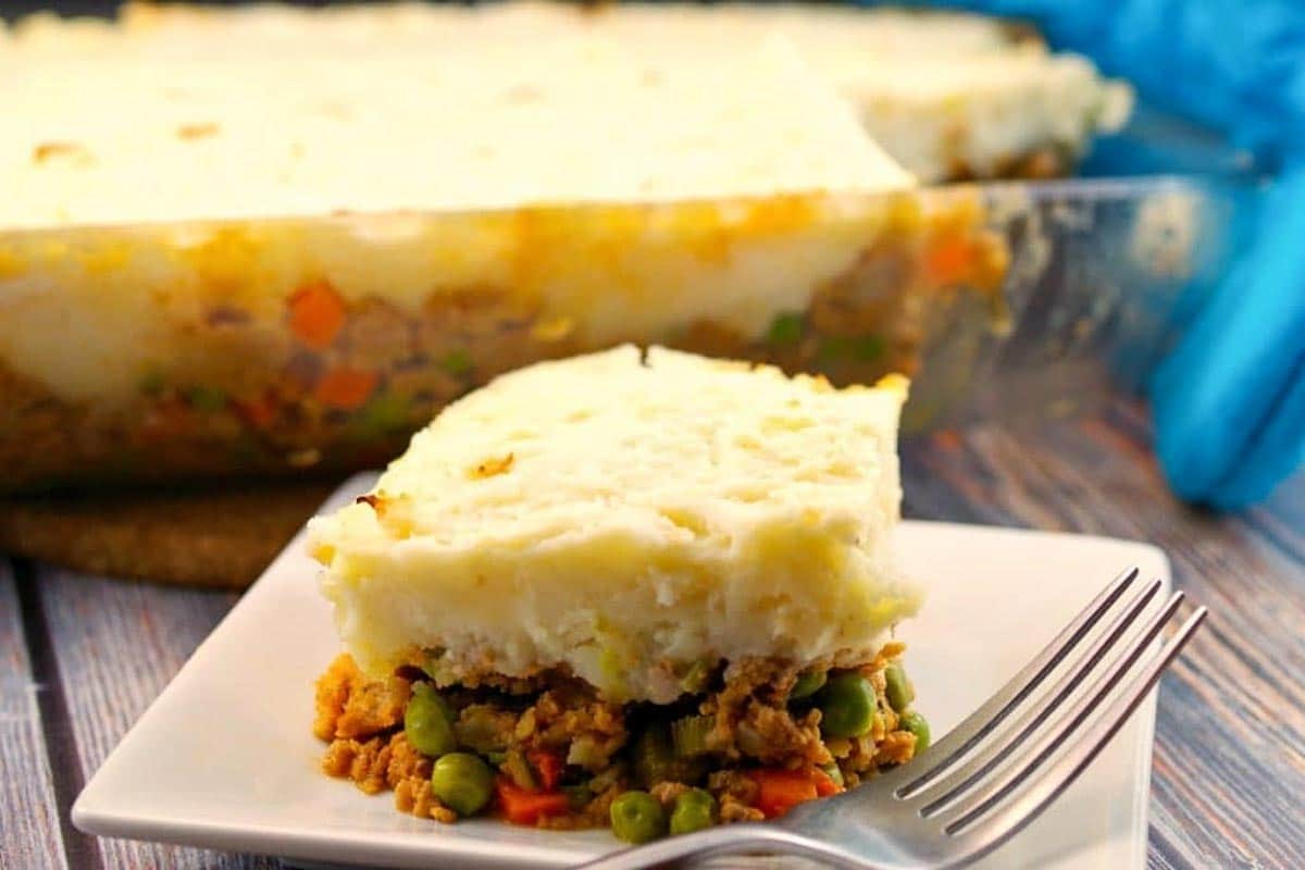 ground turkey shepherd's pie on a white plate with a fork and glass pan of ground turkey shepherd's pie in the background