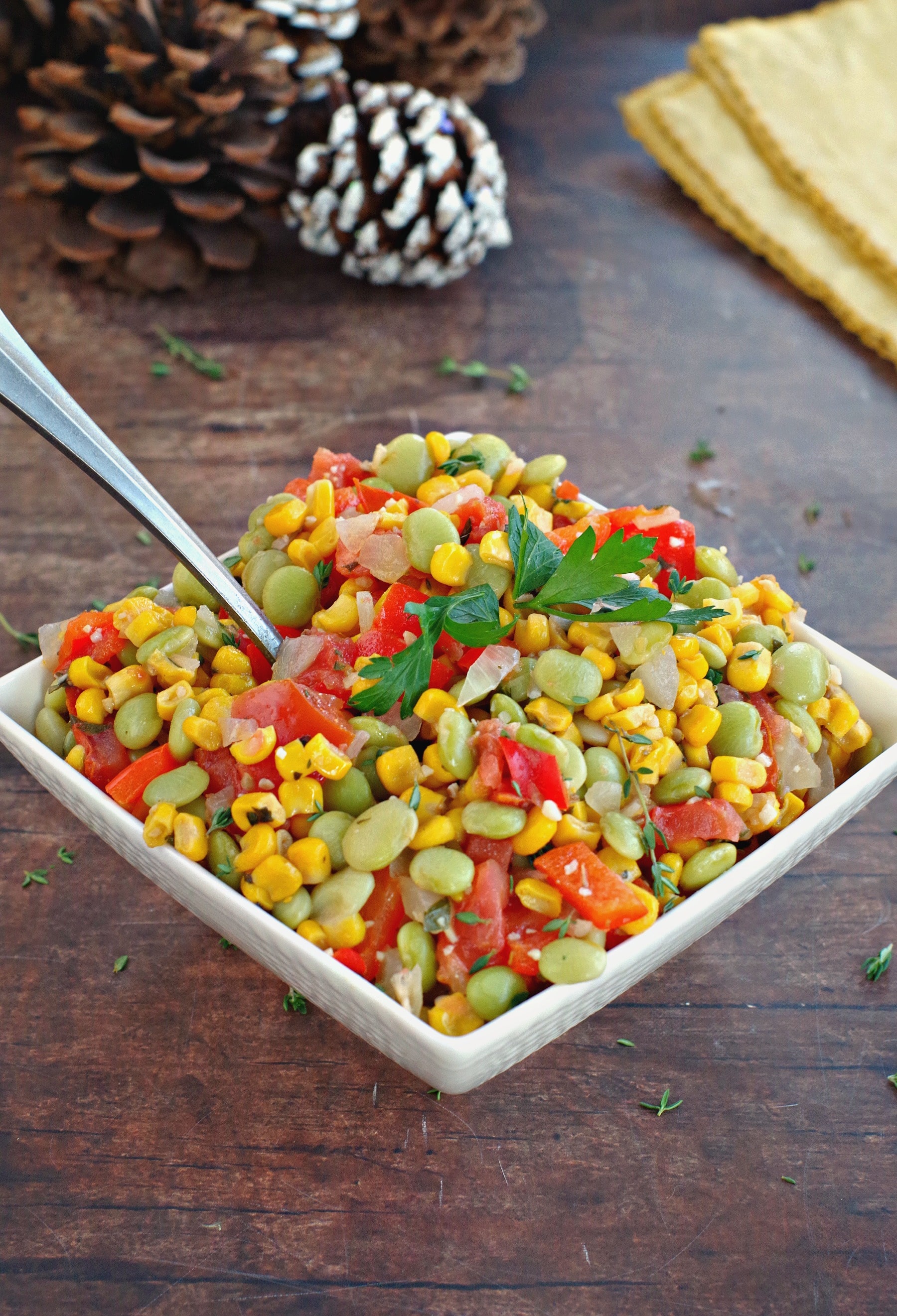 corn succotash in a white bowl with pine cones in the background