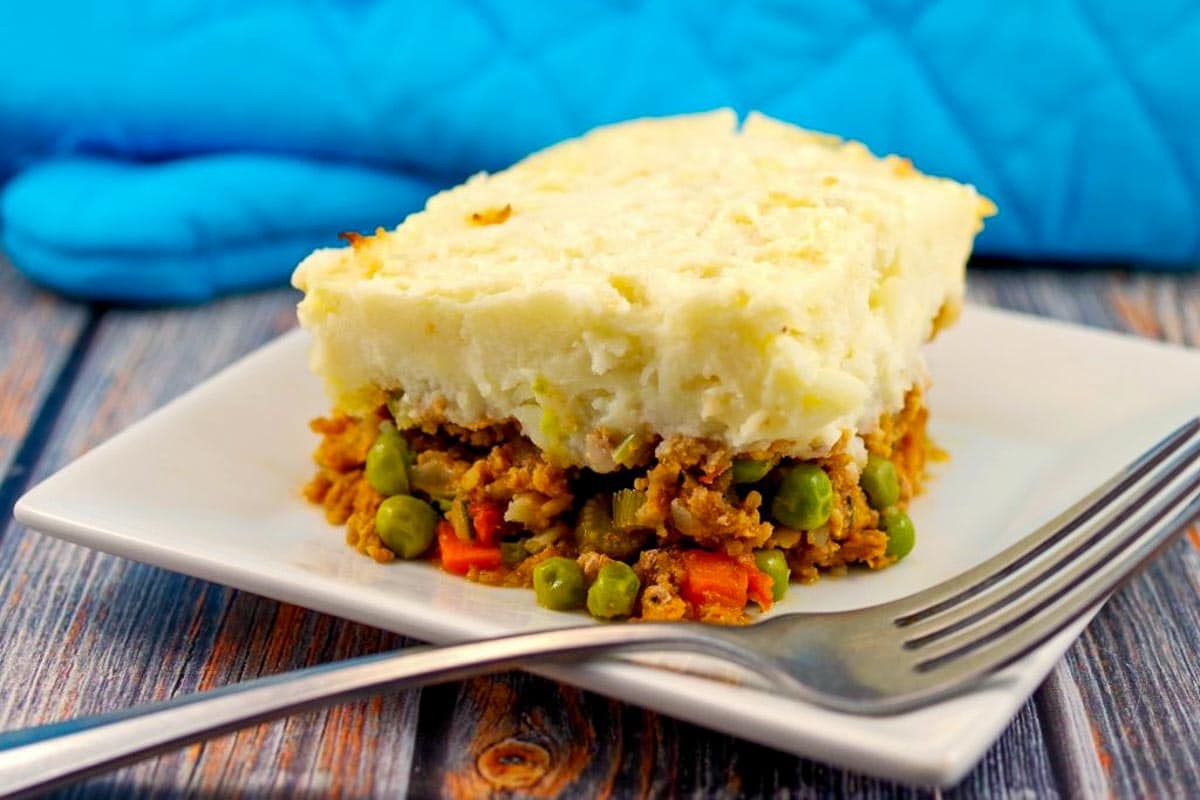 ground turkey shepherd's pie on a white plate with a fork and blue oven mitt in the background