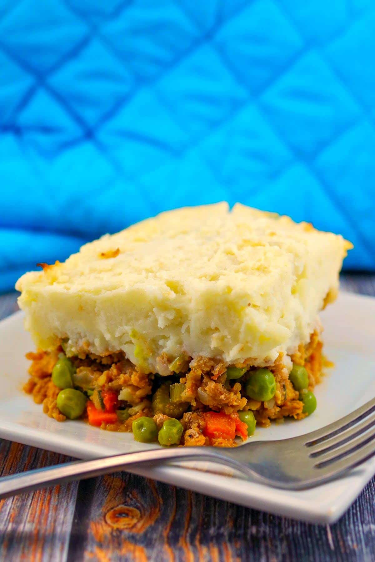 ground turkey shepherd's pie on a white plate with a fork and blue oven mitt in the background