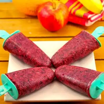 4 fruit popsicles on a white plate with fruit in background