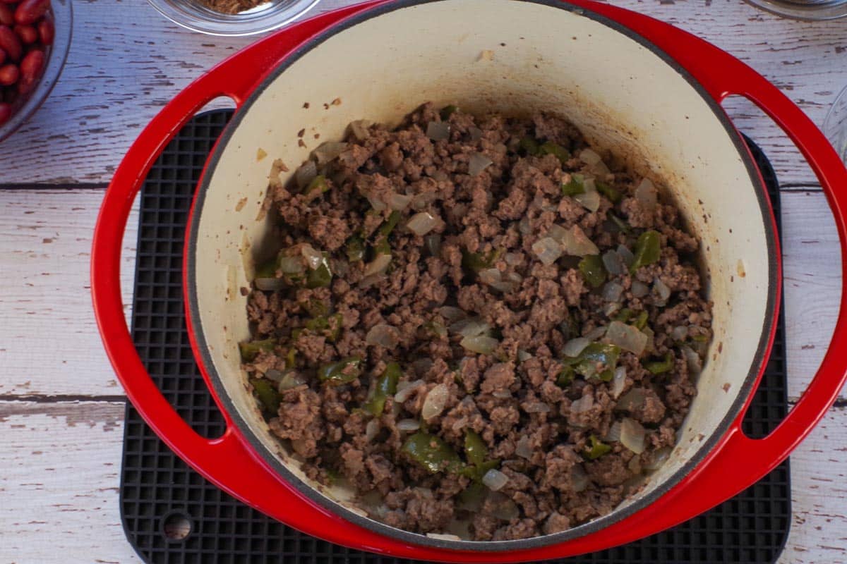 ground beef and pork with onions and green peppers browned in orange dutch oven