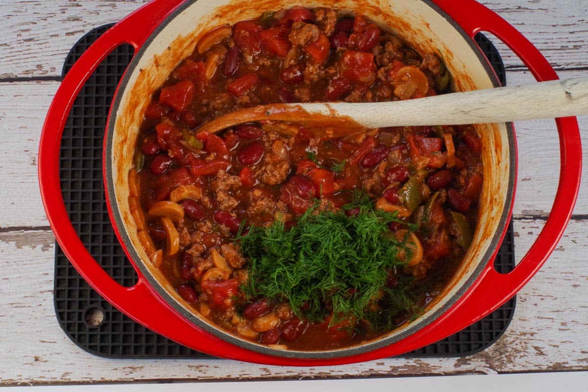 fresh dill added to beef and pork chili in orange dutch oven