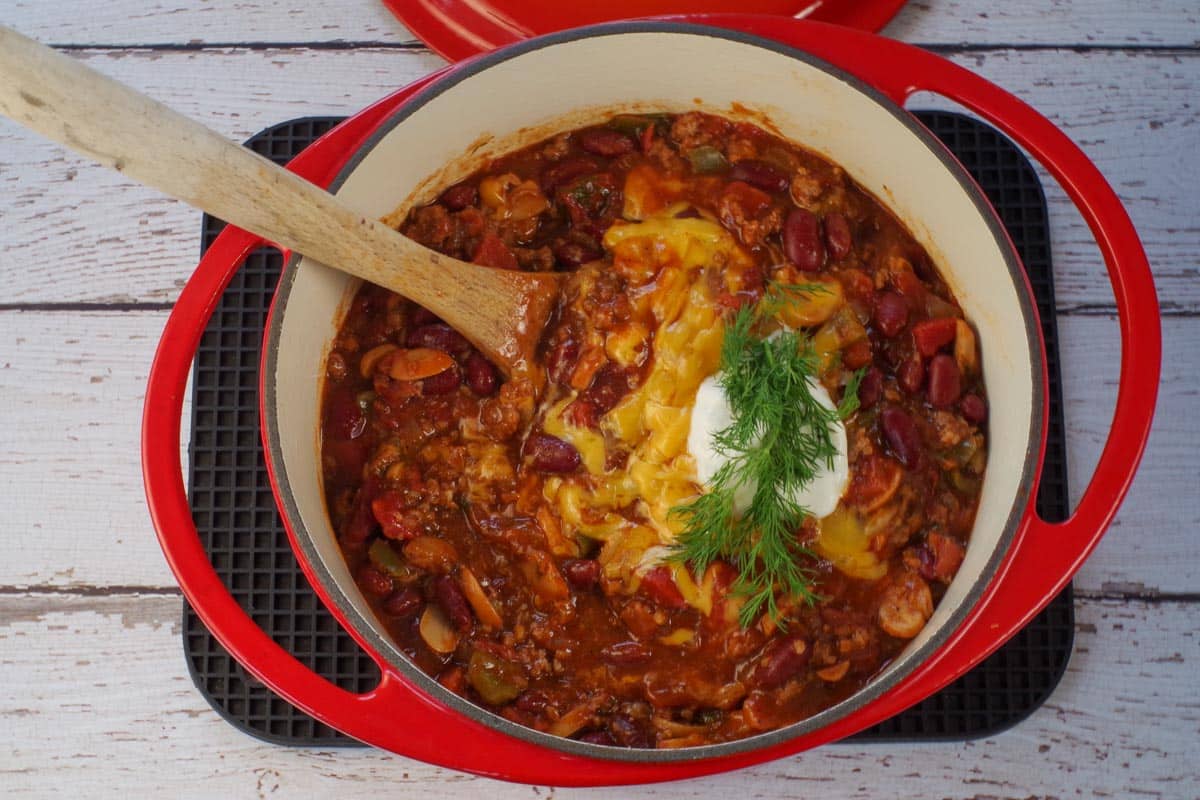 chili in orange dutch oven, garnished with cheese, dill and sour cream.