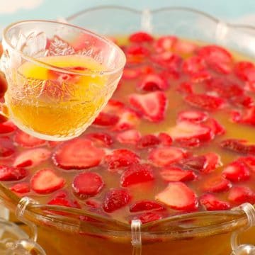 strawberry party punch in a punch bowl with a mug of punch being held up