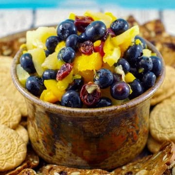 pineapple peach fruit salsa in a brown dip bowl on platter with cookies around it