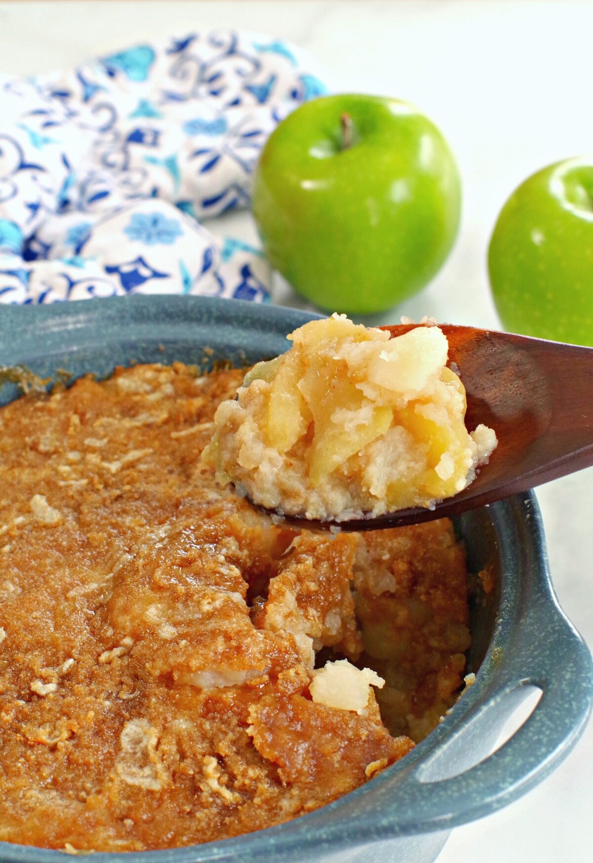 turnip and apple casserole (weight watchers friendly in a blue casserole dish, being held up on a wooden spoon with a green apple and blue patterned oven mitt in the background