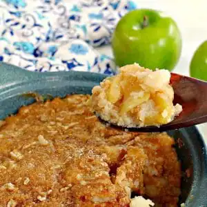 turnip and apple casserole (weight watchers friendly in a blue casserole dish, being held up on a wooden spoon with a green apple and blue patterned oven mitt in the background