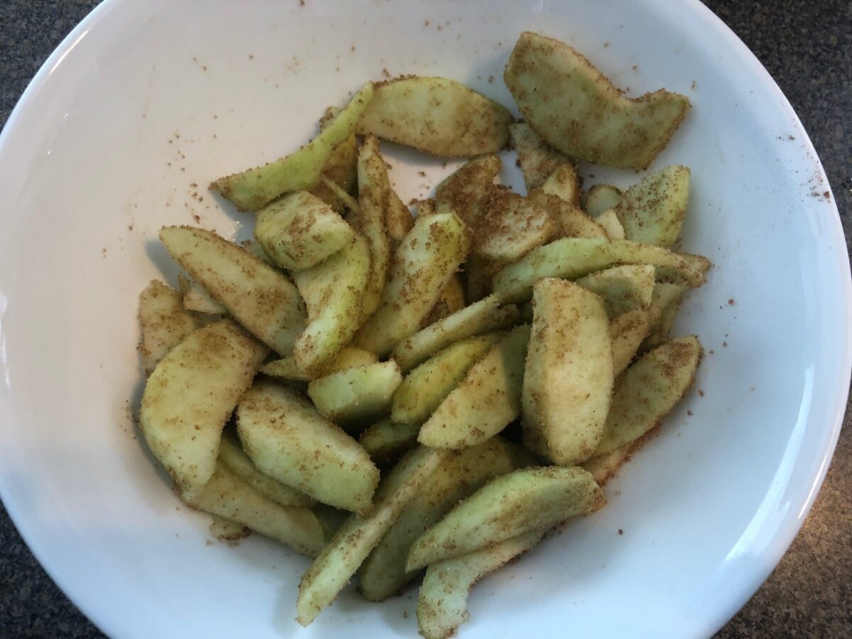 sliced apples tossed with cinnamon and sugar in white bowl