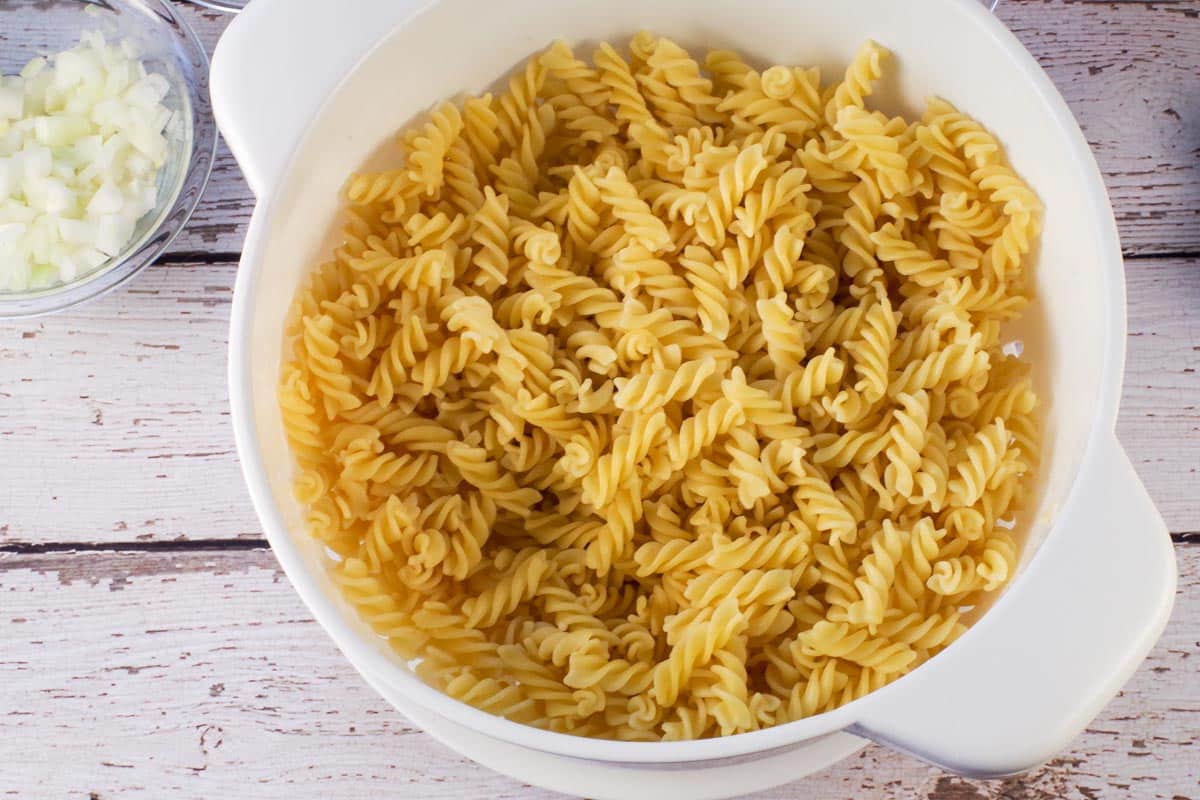 Drained pasta in colander on faux wood surface.