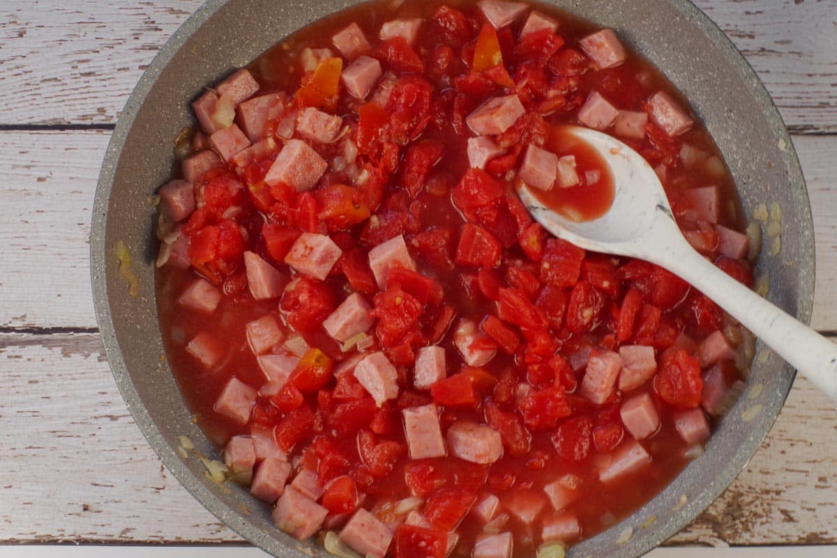 Tomatoes, garlic and chicken broth added to ham and onions.