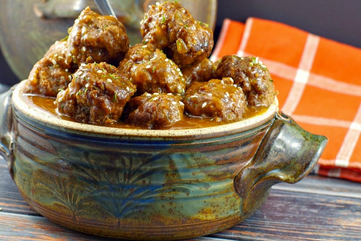 Sweet & Sour Slow Cooker Meatballs piled high in a blue grey ceramic dish with an orange and white checked tea towel in the background.