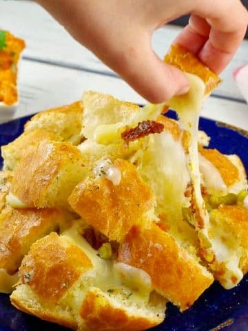 hand pulling a piece of Cheesy pull apart bread from bun