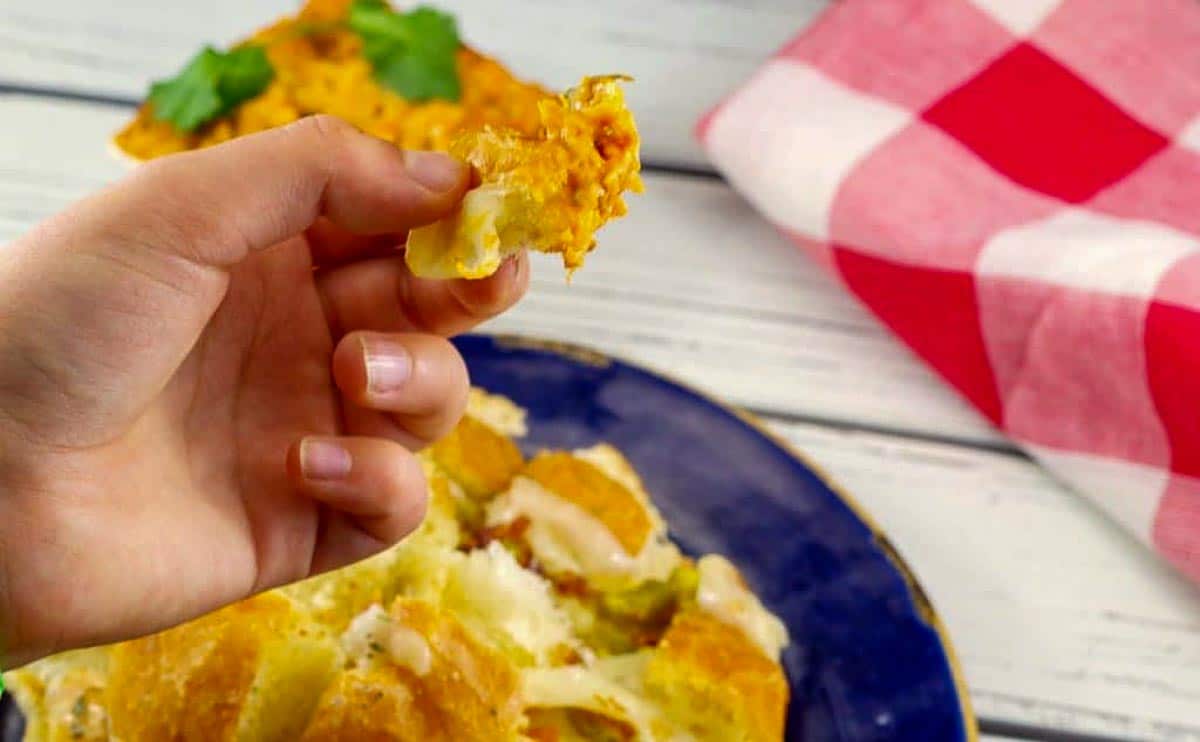 hand pulling a piece of Cheesy pull apart bread from bun, with dip on it