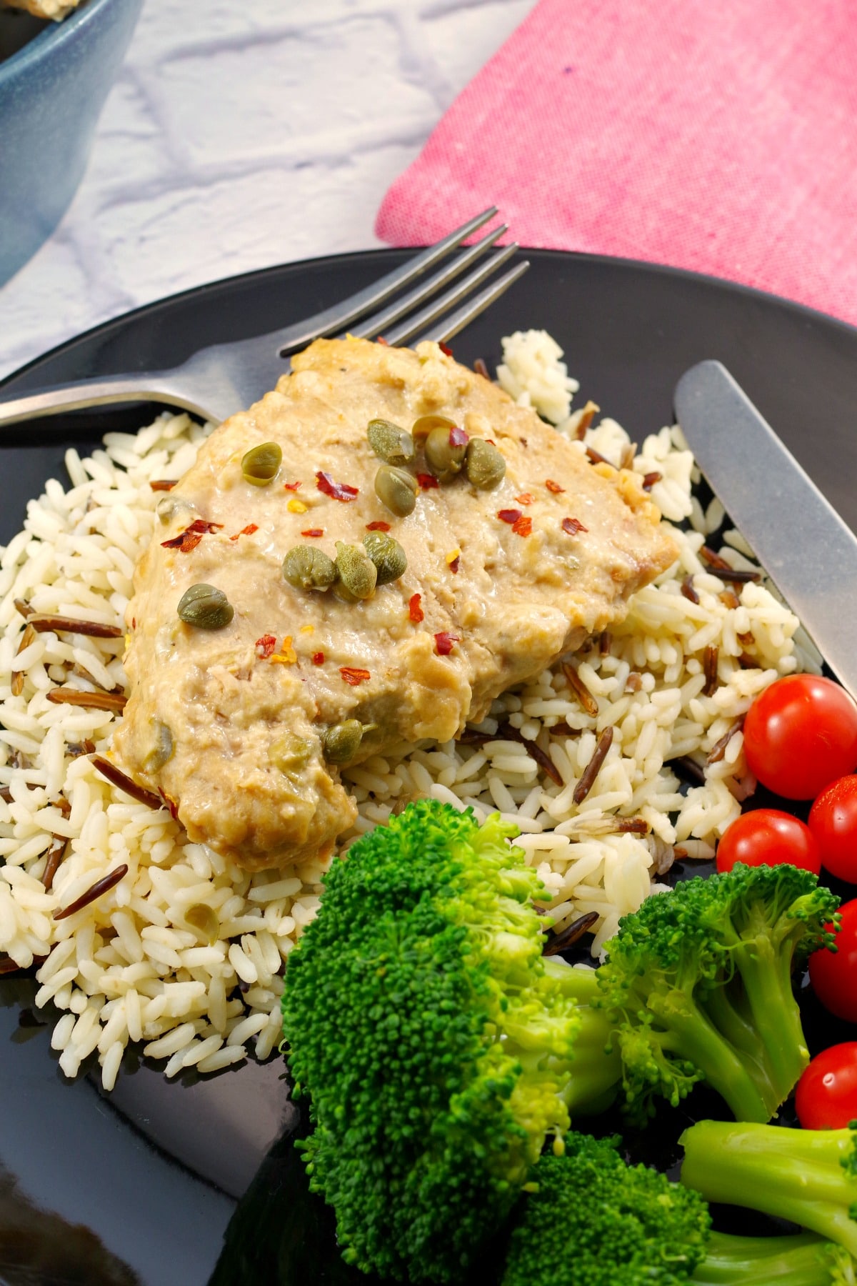 pork with creamy mustard caper sauce on a bed of rice, with salad and tomatoes on the side