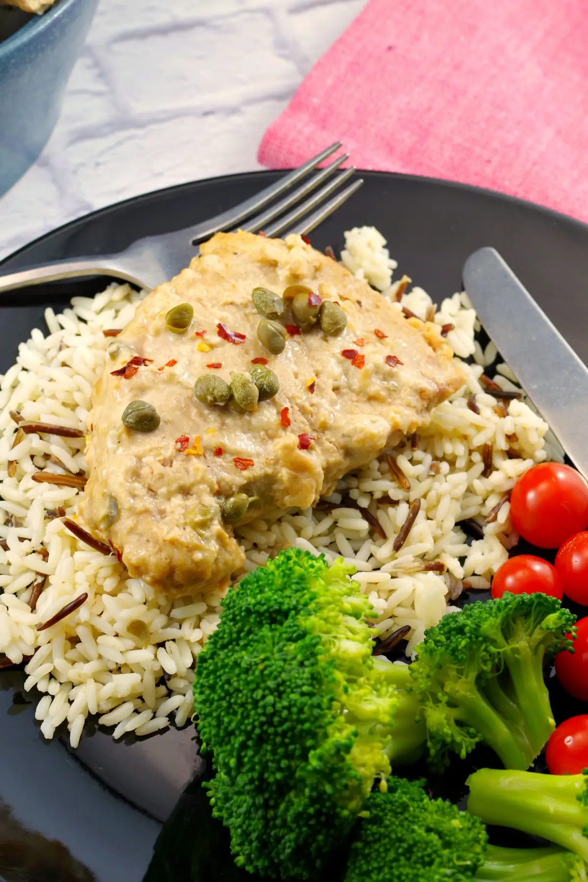 pork with creamy mustard caper sauce on a bed of rice, with salad and tomatoes on the side