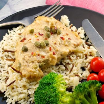 pork with creamy mustard caper sauce on a bed of rice, with salad and tomatoes on the side
