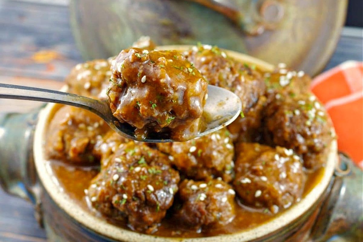 Sweet and Sour Slow Cooker Meatballs in a ceramic dish with one meatball being held up with a spoon.