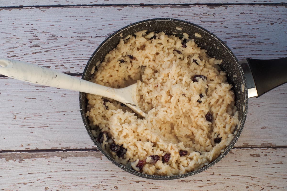 All ingredients in rice pudding cooked in pot with large spoon.