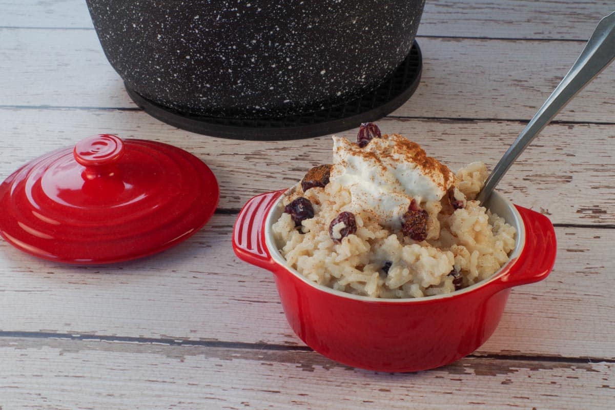 Cranberry Rice Pudding in a red individual serving dish with a lid and pot of more rice pudding in the background.