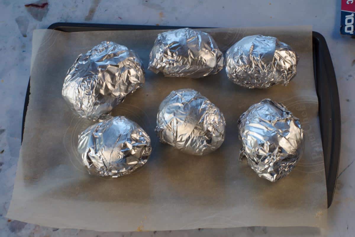 6 Potatoes wrapped in foil on a parchment lined baking sheet