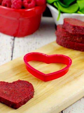 healthy jello hearts on cutting board with raspberries and spinach in the background