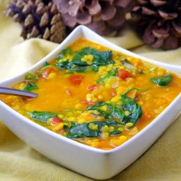 red lentil and spinach soup in a white bowl on yellow linens with pine ones in the background