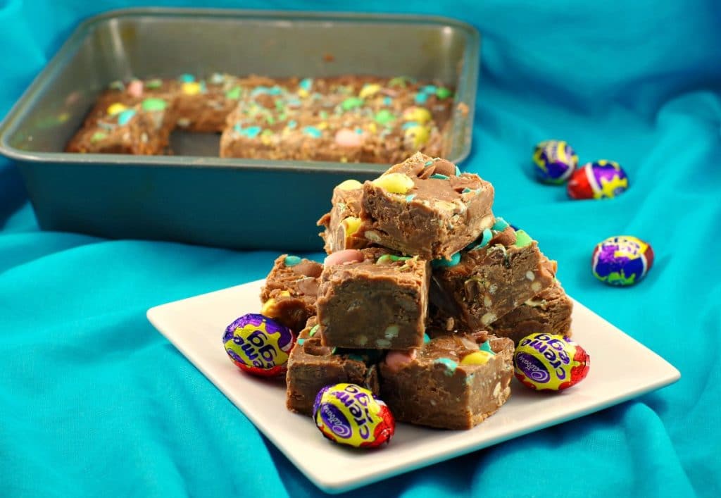 Microwave mini Easter Creme egg fudge stacked on plate with fudge in pan in background