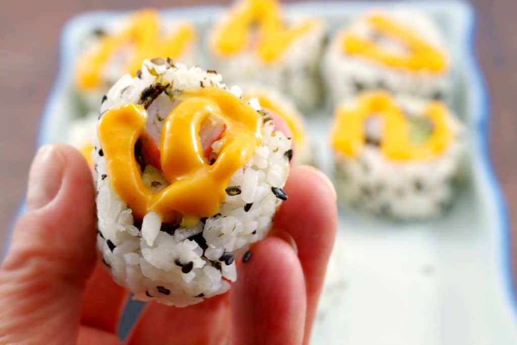Close up of California Roll with swirl of sriracha mayonnaise on top and additional rolls in the background