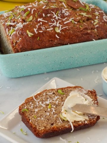 banana bread in blue loaf pan with slice of banana bread on a white plate with butter