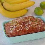 Tropical banana bread in blue loaf pan with bananas and limes in background
