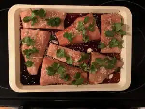 frozen raw salmon fillets on sheet pan with soya sauce, cilantro, sesame seeds and ginger
