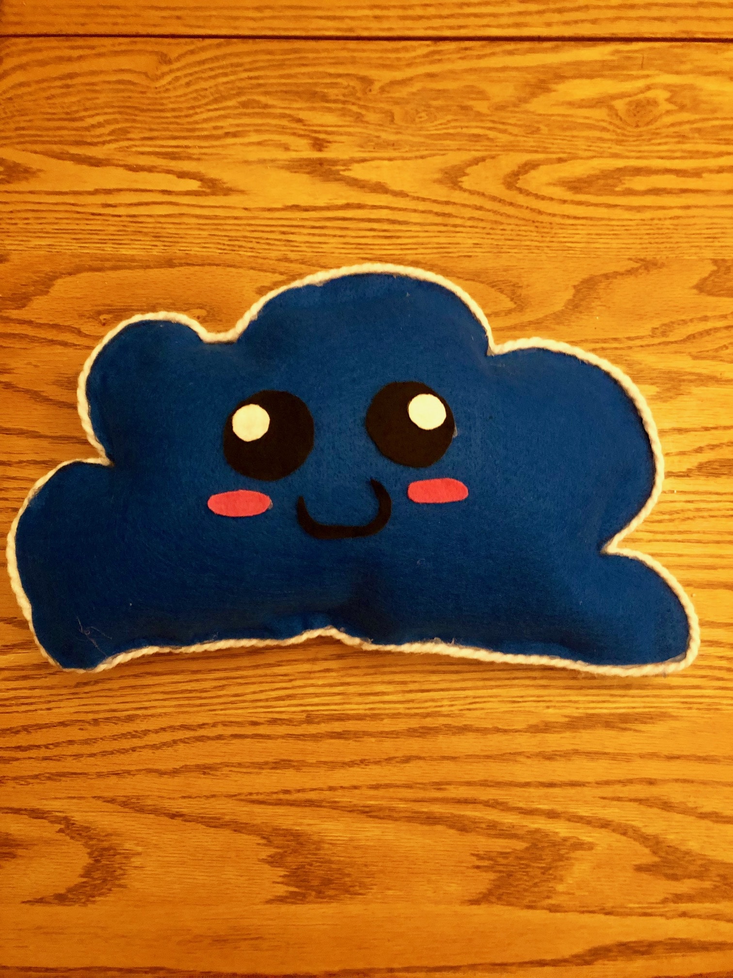 Blue stuffed cloud pillow with white lining and a smiley face and pink cheeks