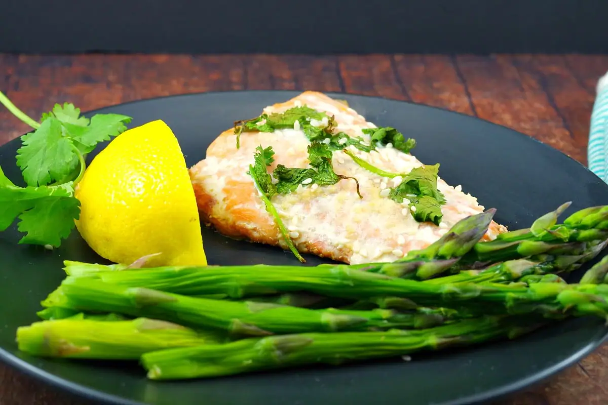 Salmon fillet on a black plate with lemon wedge and steamed asparagus