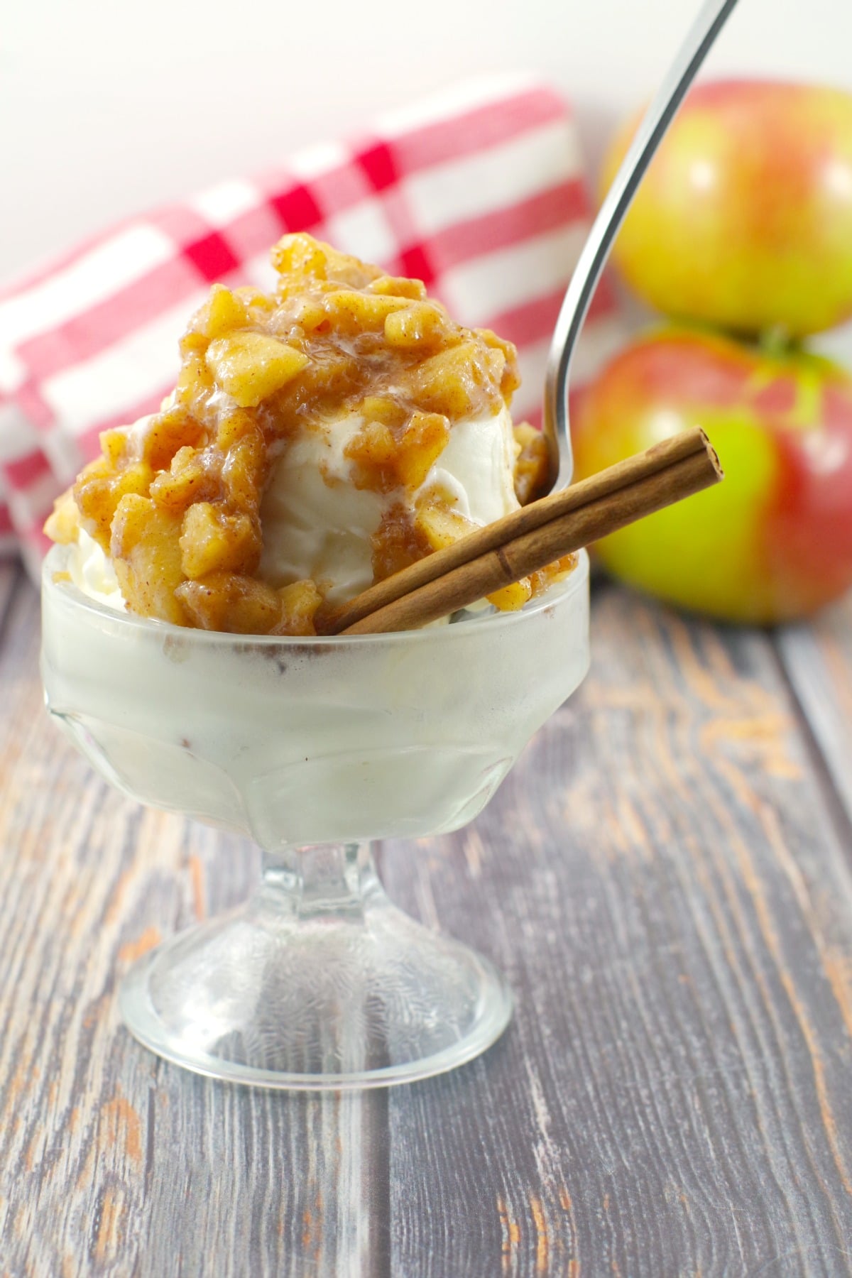 apple cinnamon topping on frozen yogurt in ice cream dish with spoon and cinnamon stick, apple and checked cloth in background