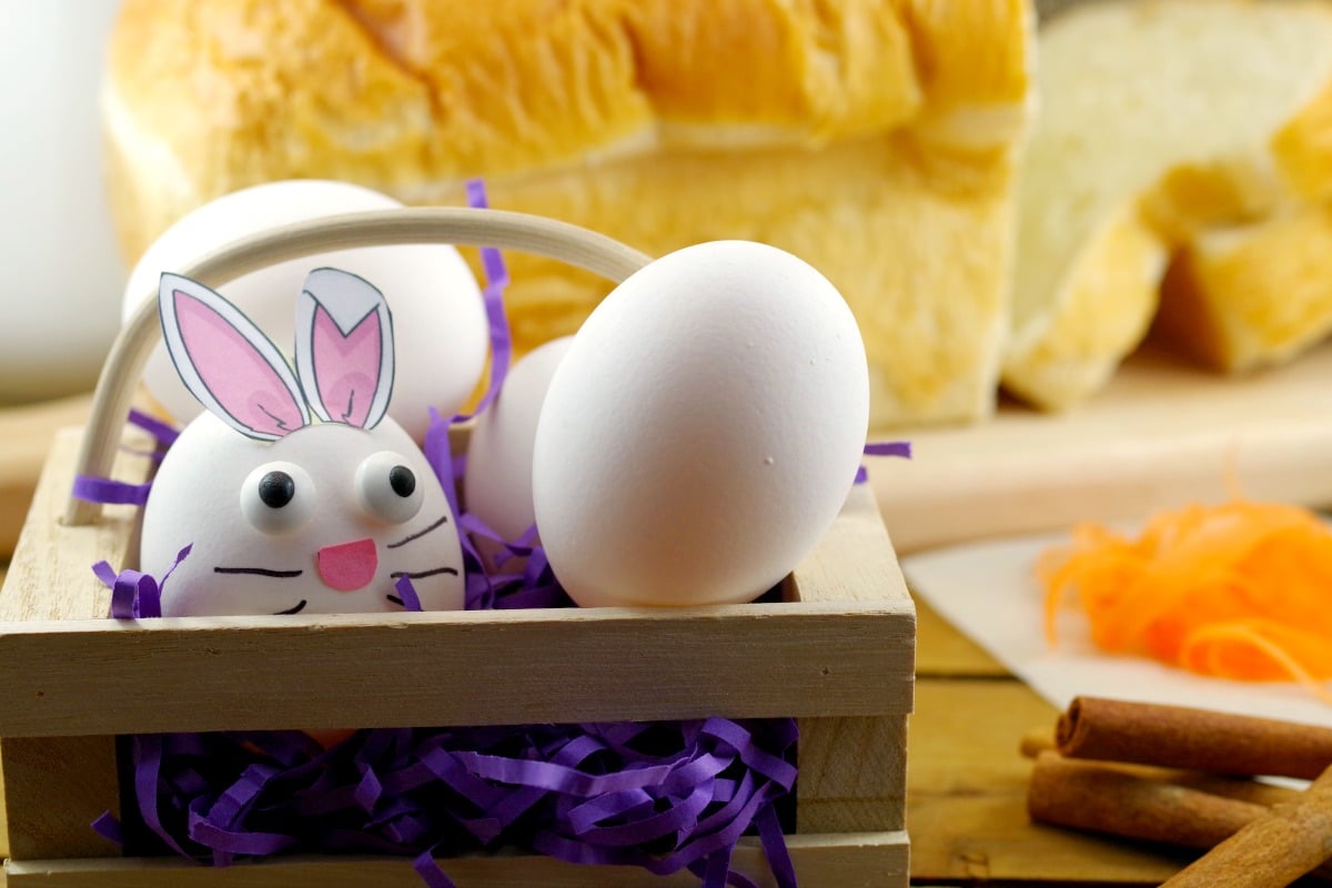 3 Eggs in a basket (one made to look like an Easter bunny) with bread and other french toast ingredients in background