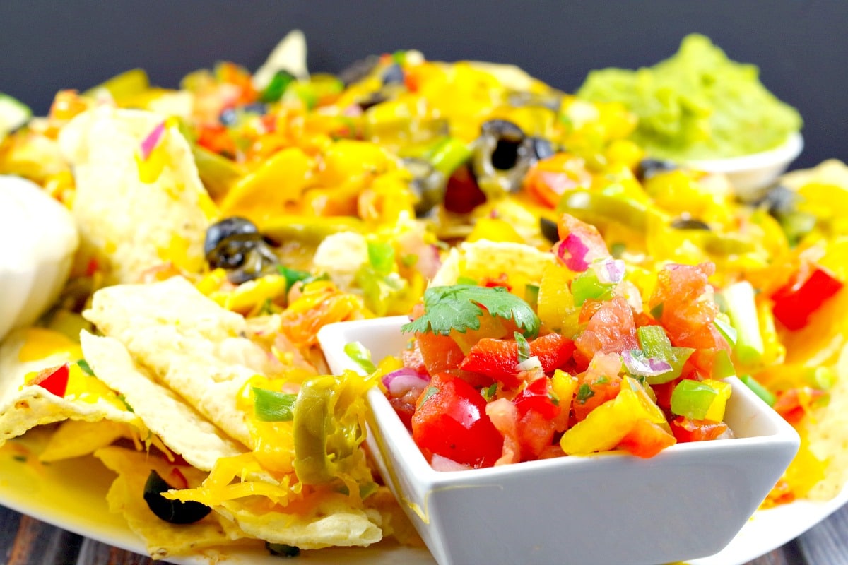 Pico de Gallo Salsa on plate of nachos (with the works) and a small white dipping bowl of salsa in the foreground