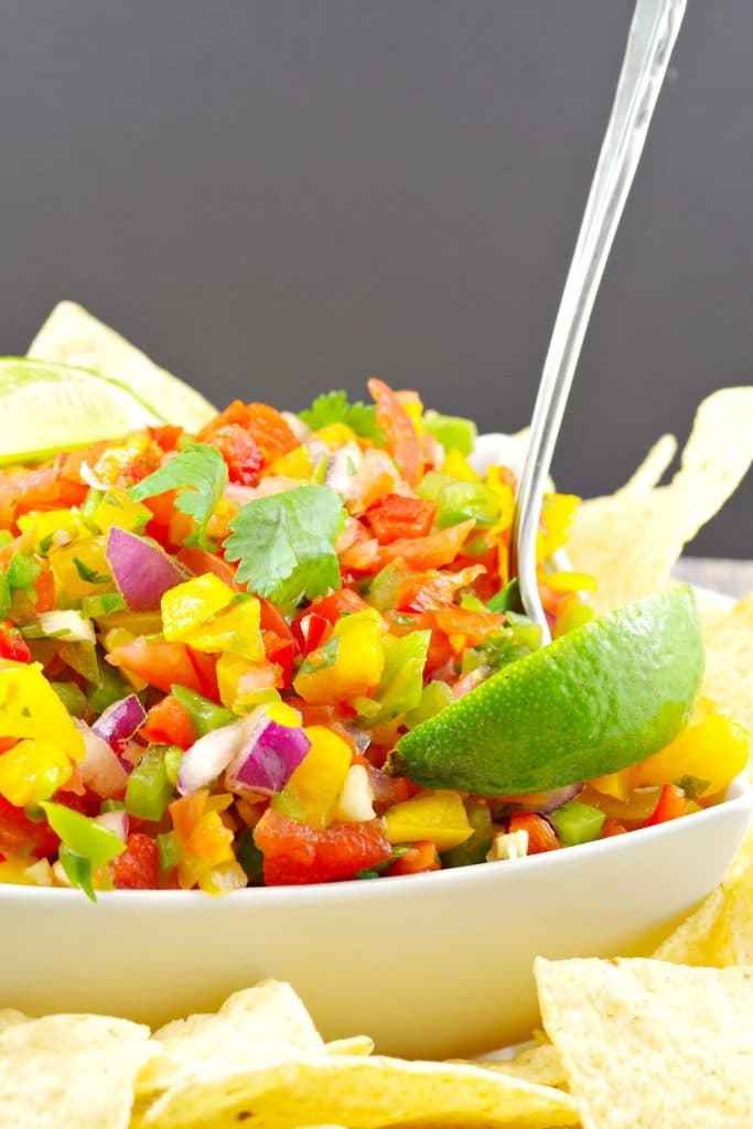 Pico de Gallo Salsa. garnished with 2 lime wedges, in a white bowl surrounded by nacho chips