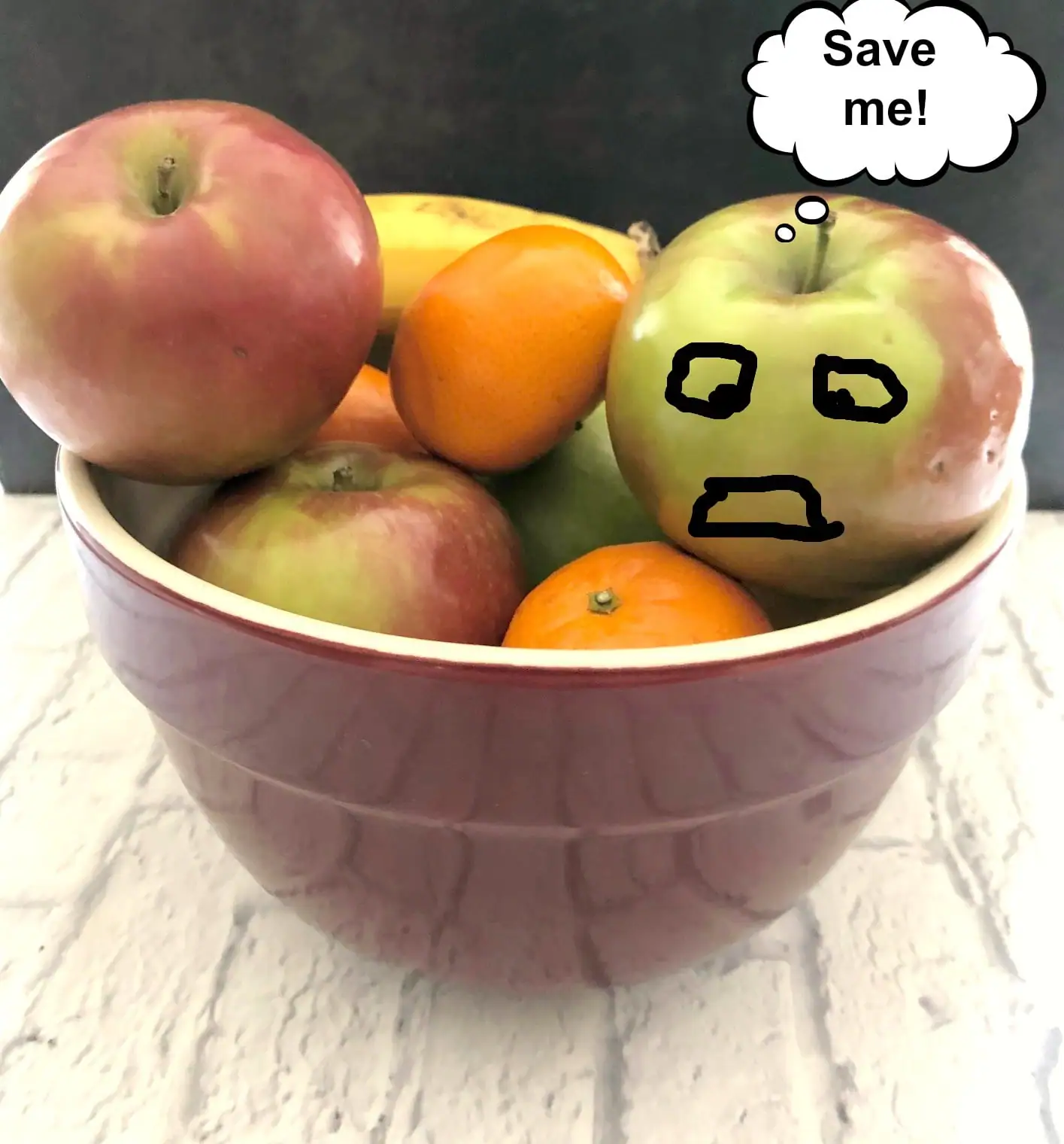 Fruit in a bowl with a word bubble from the apple saying 'save me' and black hand drawn distressed face on apple