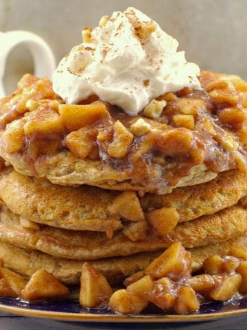 stacked pancakes with apple topping and whipped cream