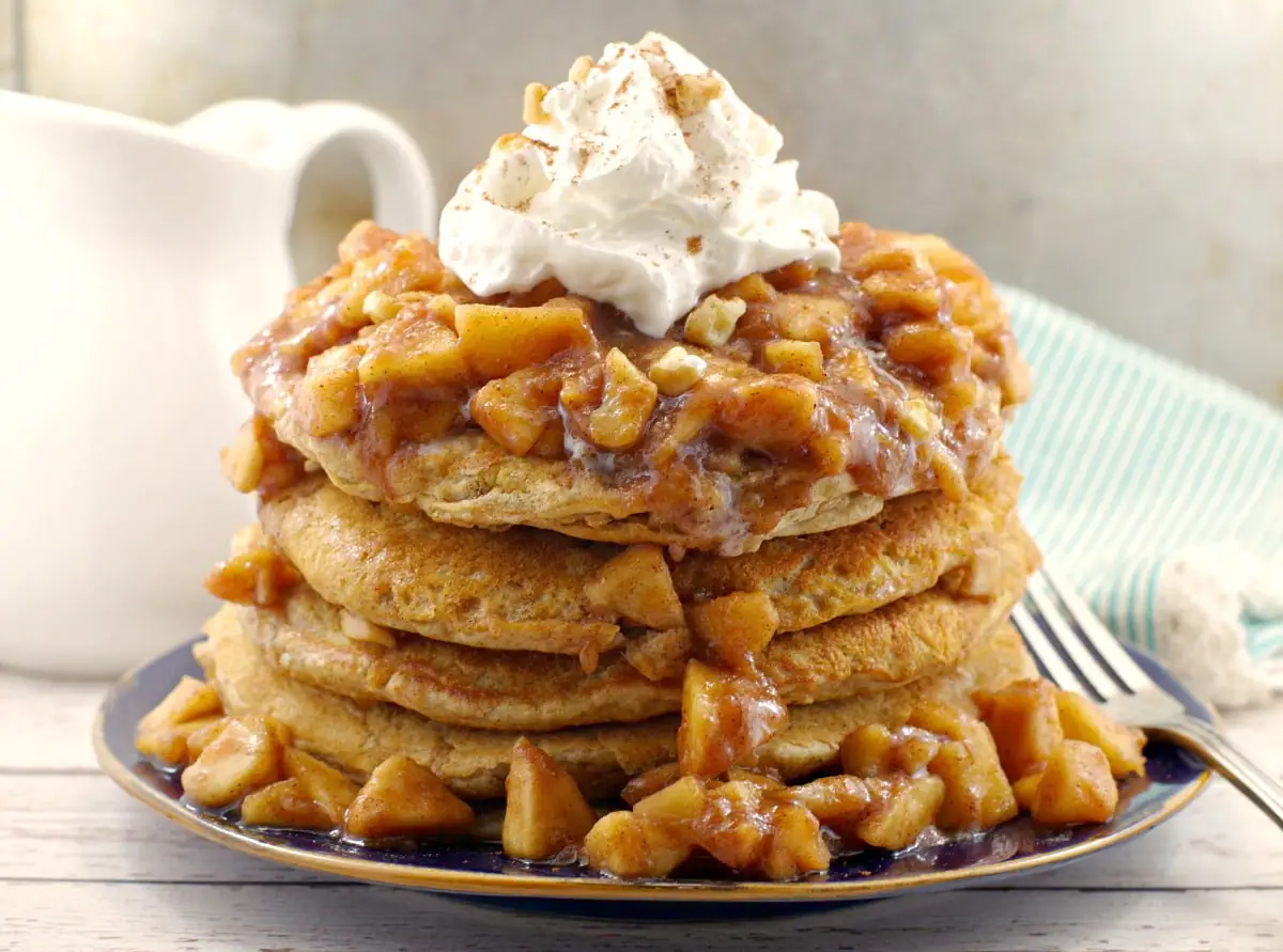 stacked pancakes with apple topping and whipped cream