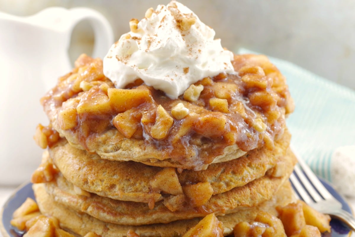 close up of stacked pancakes with apple topping and whipped cream