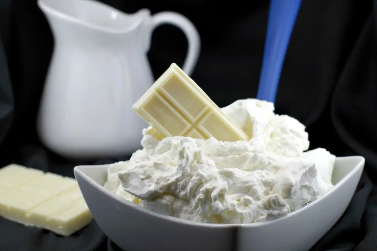 A bowl of white chocolate whipped cream frosting with a bar of baker's white chocolate stuck in frosting
