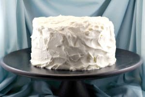 whole cake on black cake stand, covered with white chocolate whipped cream frosting