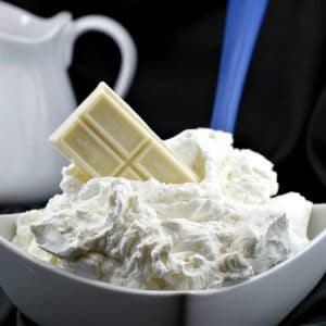 A bowl of white chocolate whipped cream frosting with a bar of baker's white chocolate stuck in frosting