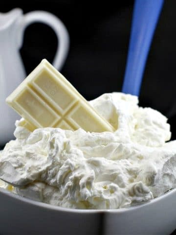 A bowl of white chocolate whipped cream frosting with a bar of baker's white chocolate stuck in frosting