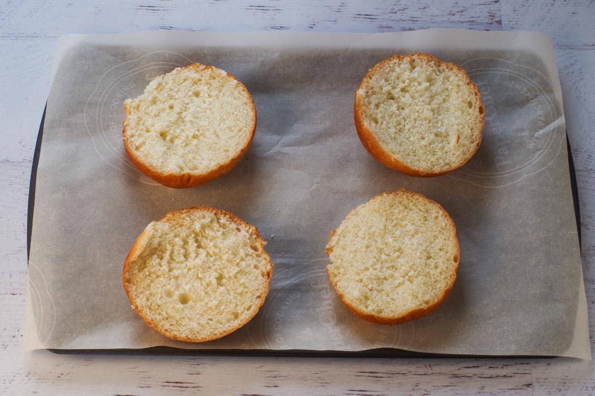 Kaiser buns cut in half on a parchment lined baking sheet